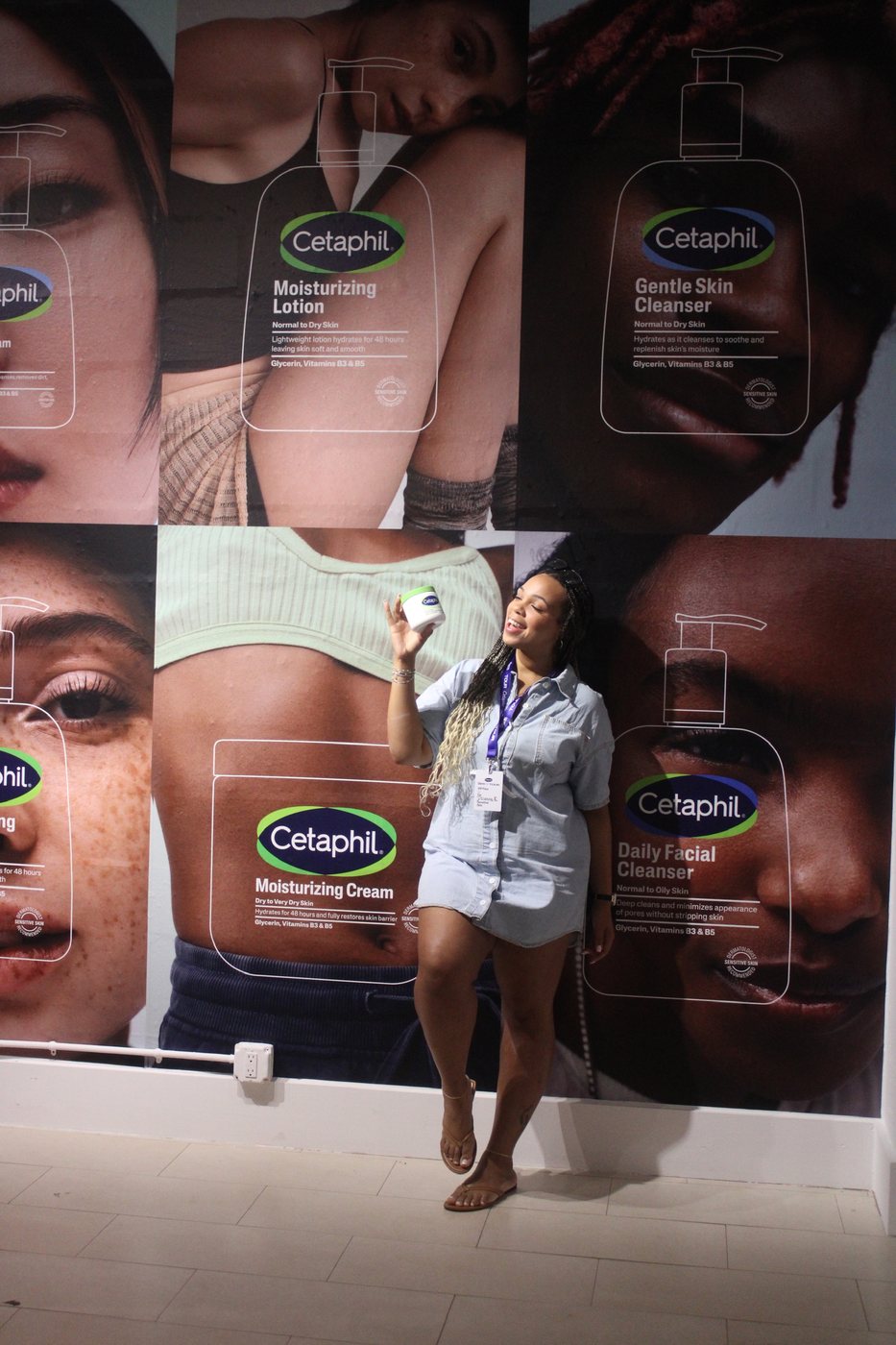 Delanna holding a Cetaphil jar in front of a wall of Cetaphil posters