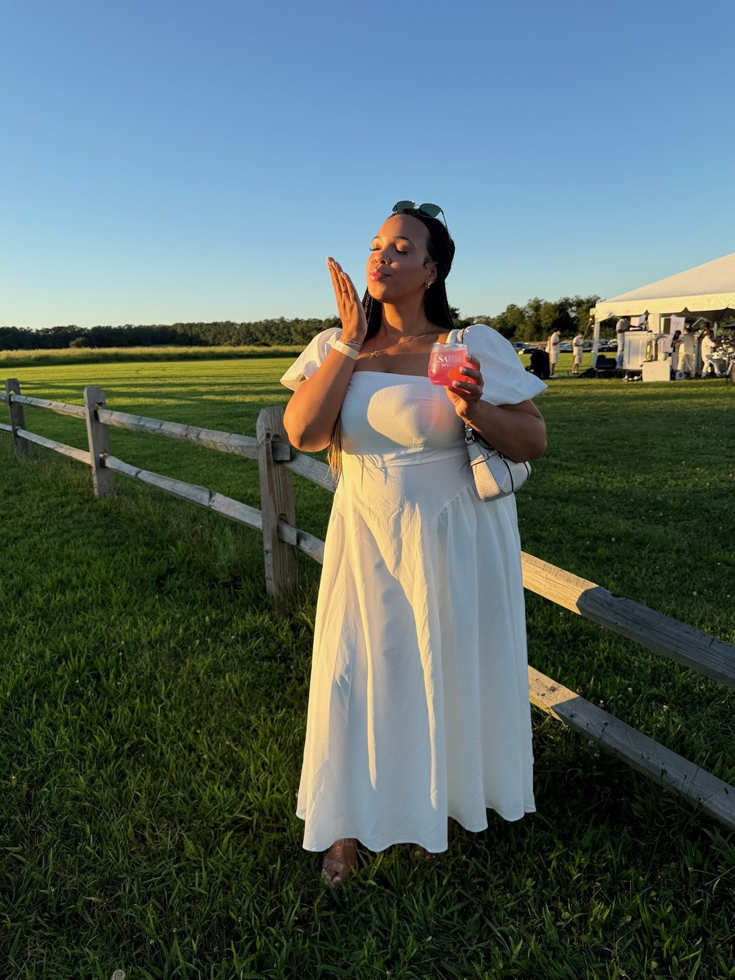 Delanna blowing a kiss in a white dress at an outdoor evening event