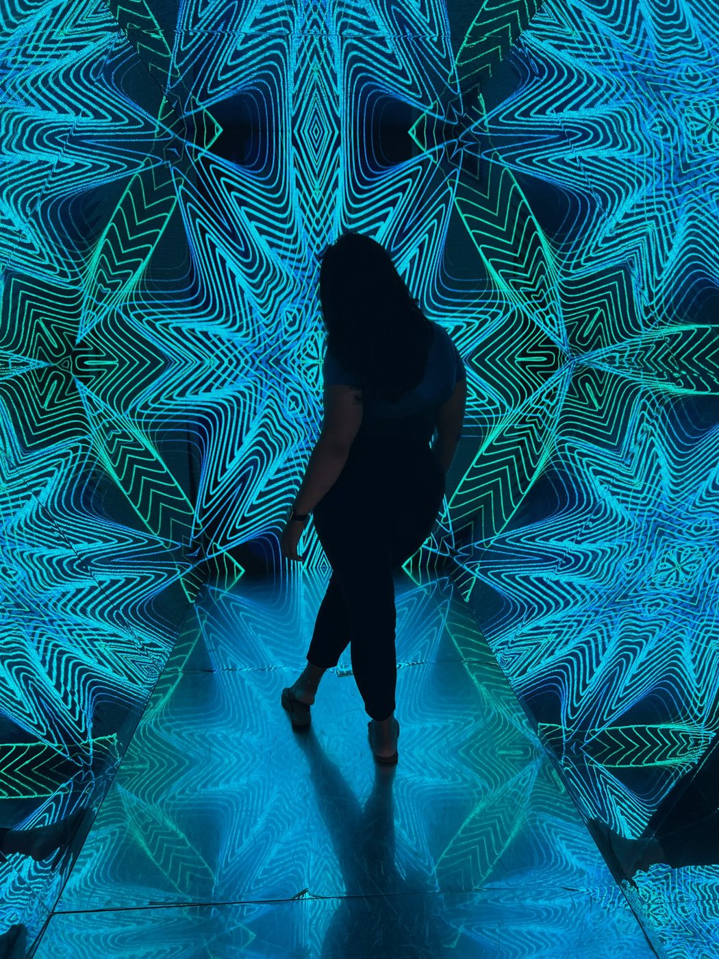 Delanna standing in a glowing blue mirrored art installation