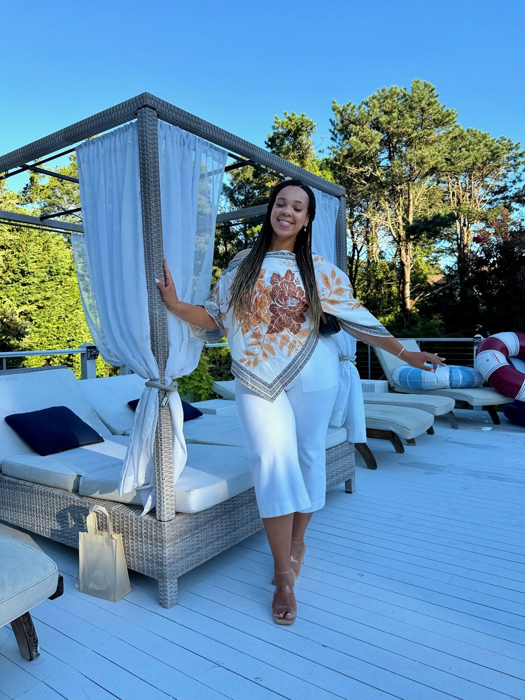 Delanna in a printed white set beside a canopy daybed on a resort deck
