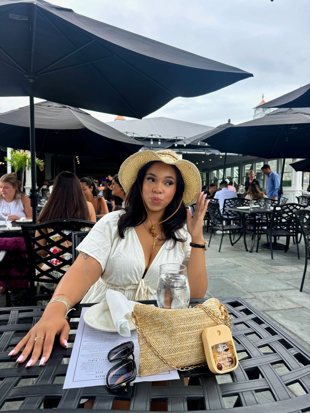 Delanna at a rooftop restaurant table in a straw hat and white dress