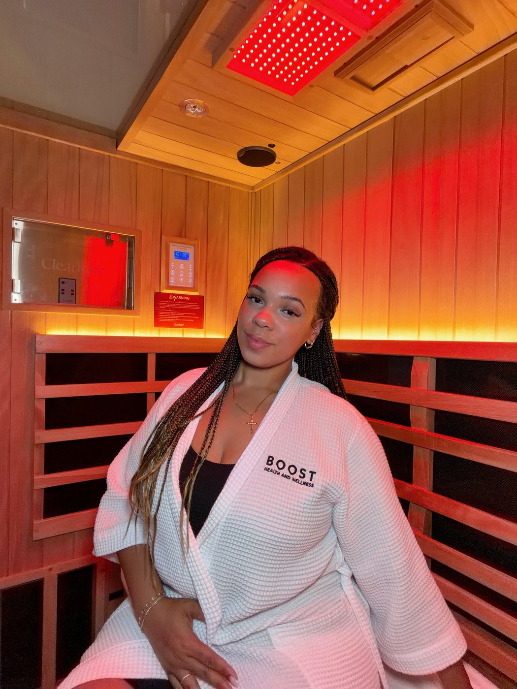 Delanna in a white robe inside a red-light infrared sauna