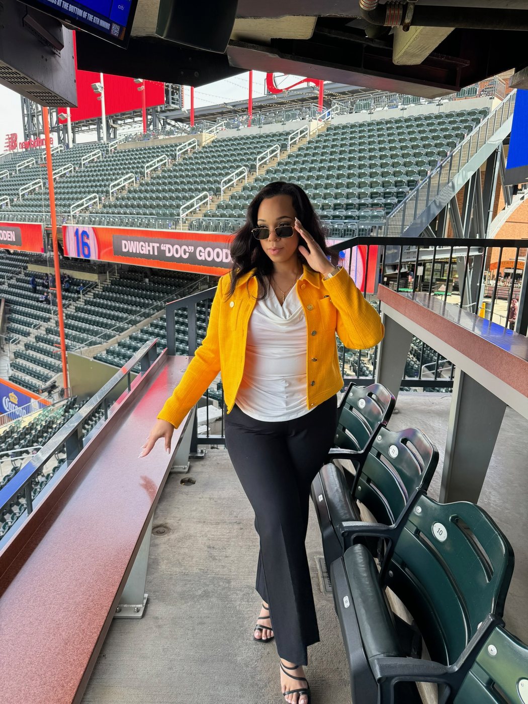 Delanna in a yellow jacket walking through the stands of a ballpark